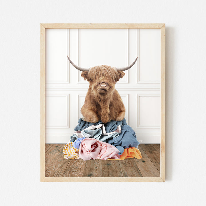 a picture of a highland cow sitting on a pile of clothes