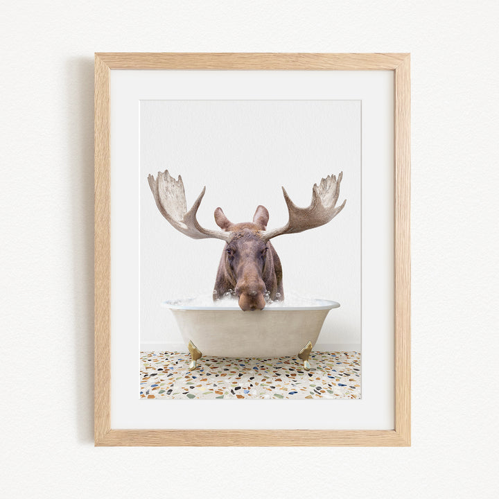 A moose with large antlers is sitting in a white bathtub, with a mosaic floor in the background.