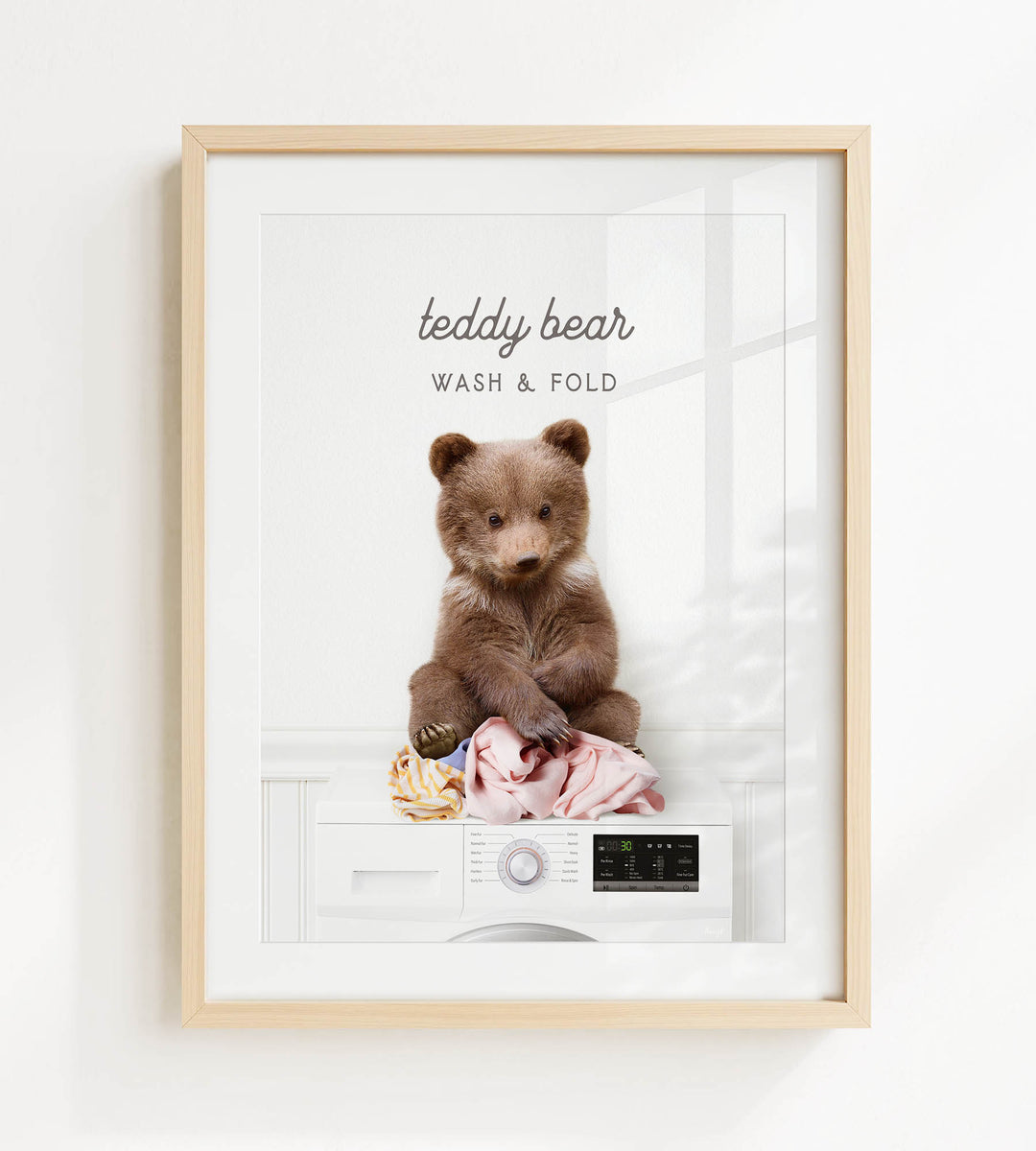 A framed image of a teddy bear sitting on a pile of laundry, with the text "teddy bear WASH & FOLD" above it.