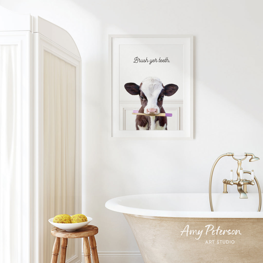 a bathroom with a white bathtub, a wooden stool, and a framed picture of a cow holding a toothbrush.
