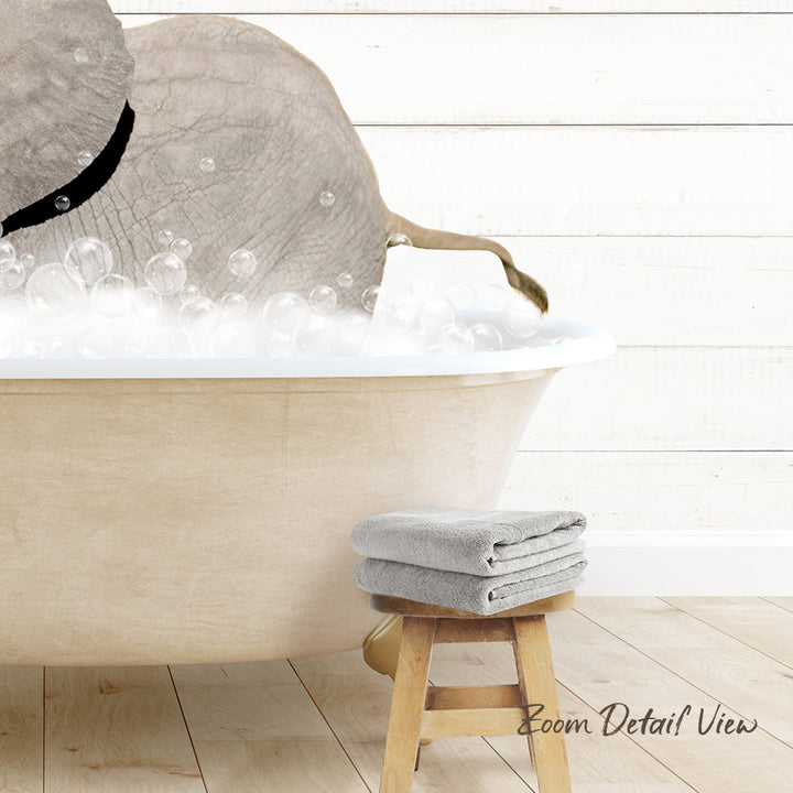 A bathtub filled with bubbles, with a gray elephant standing inside it. Next to the bathtub is a wooden stool with a towel on it.