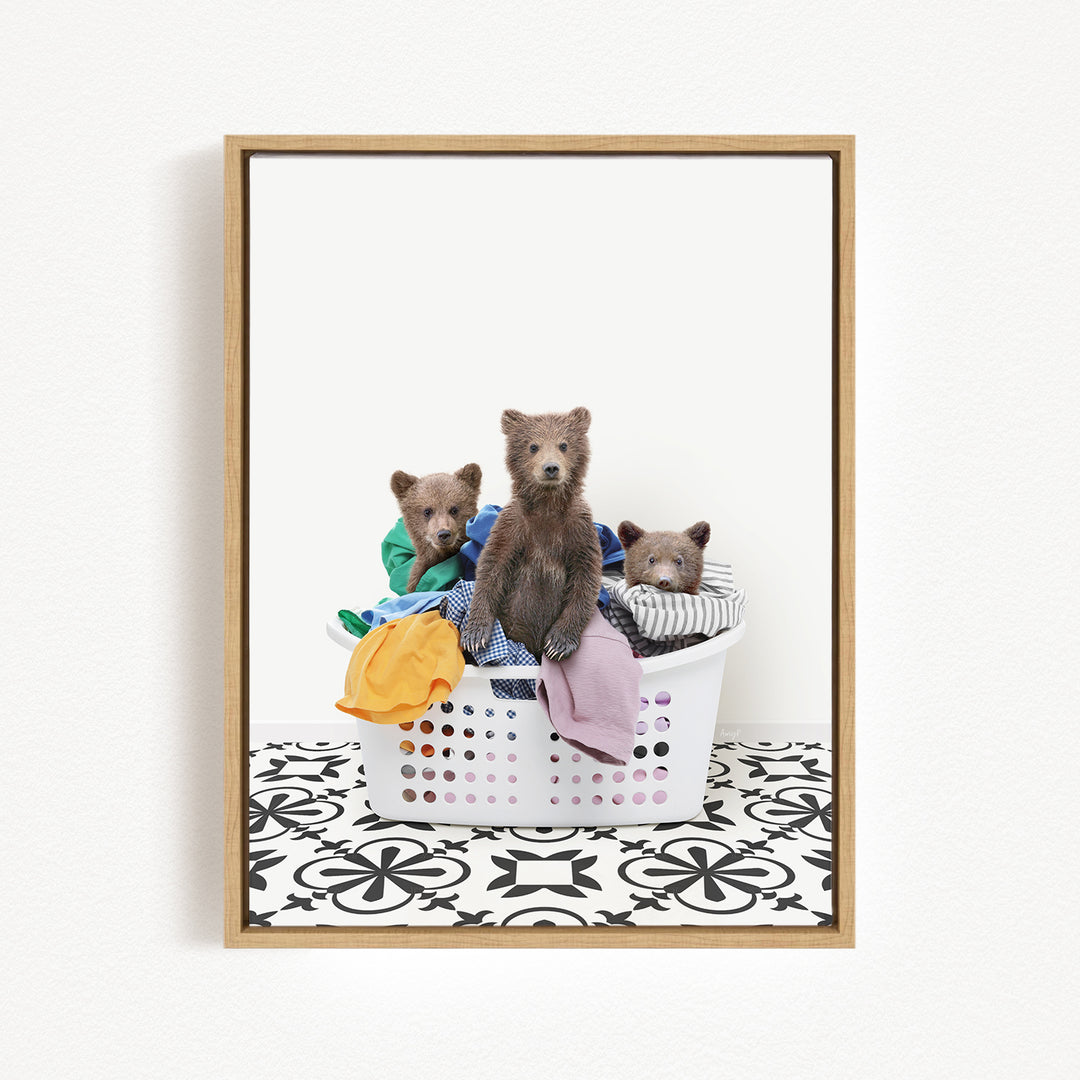 A framed image showing three bears sitting in a laundry basket filled with clothes.
