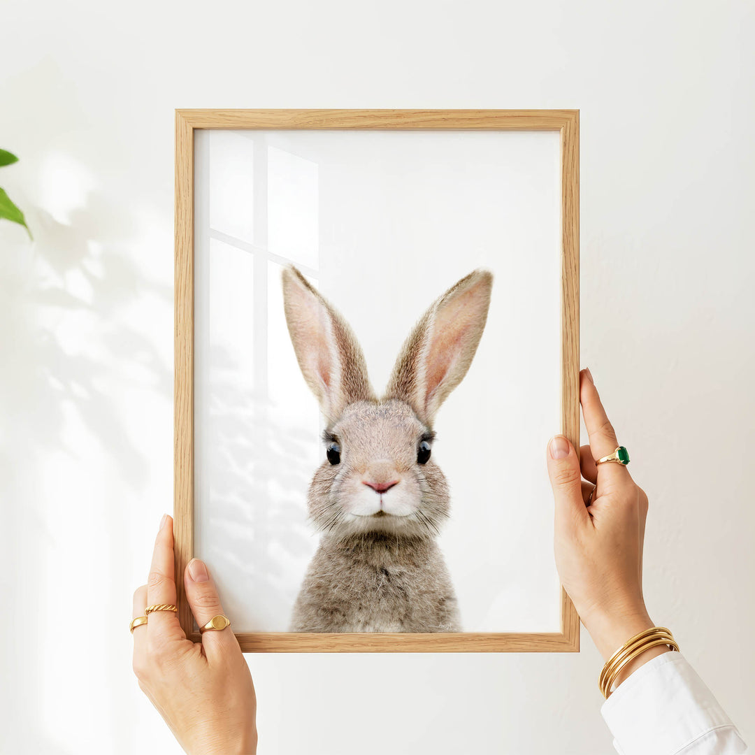 A person's hands are holding a wooden frame with a picture of a rabbit inside it.