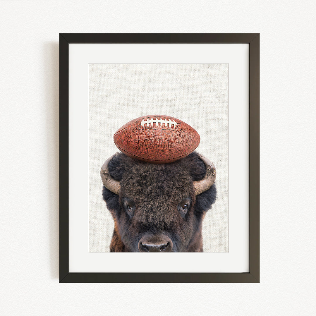 A buffalo with a football resting on its head, in a framed artwork.