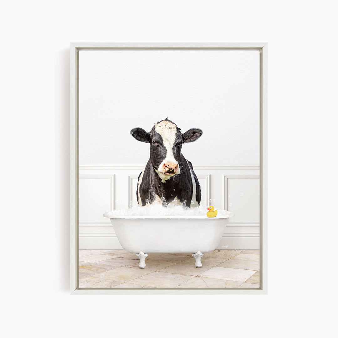 A black and white cow standing in a white bathtub, with a yellow rubber duck floating in the water.