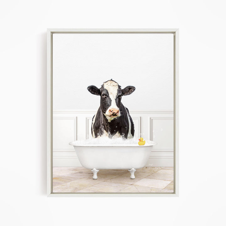 A black and white cow standing in a white bathtub, with a yellow rubber duck floating in the water.