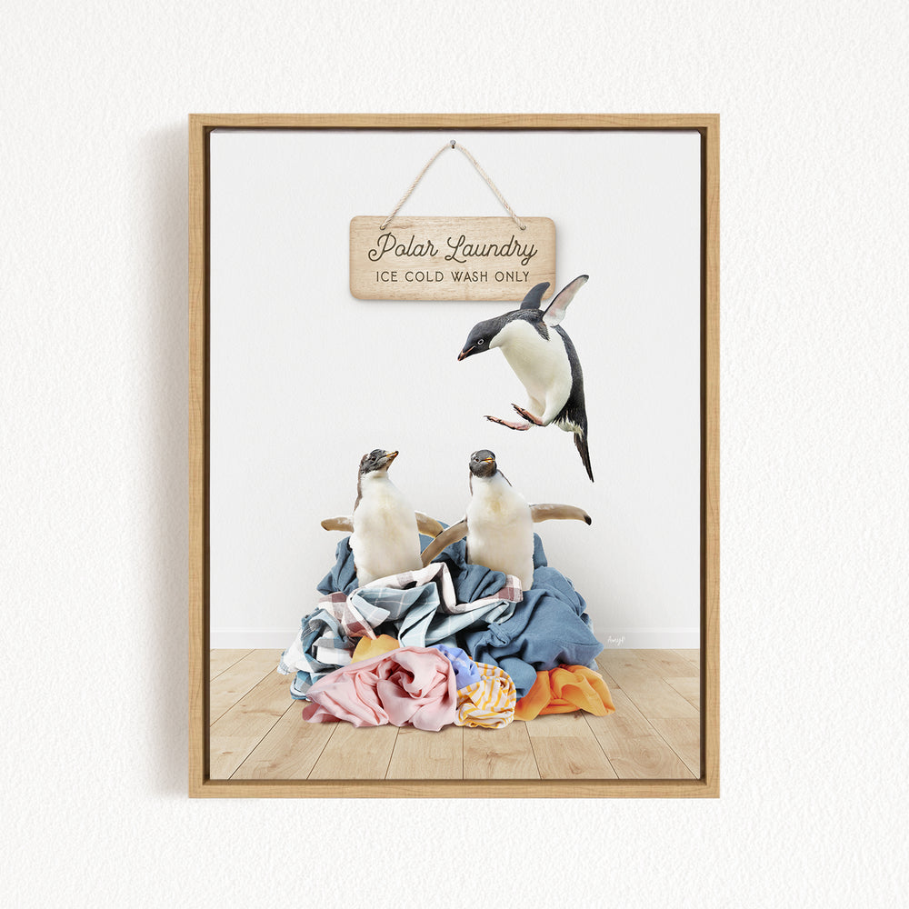 A framed image depicting three penguins standing on a pile of clothes, with a sign hanging above them that reads "Polar Laundry".