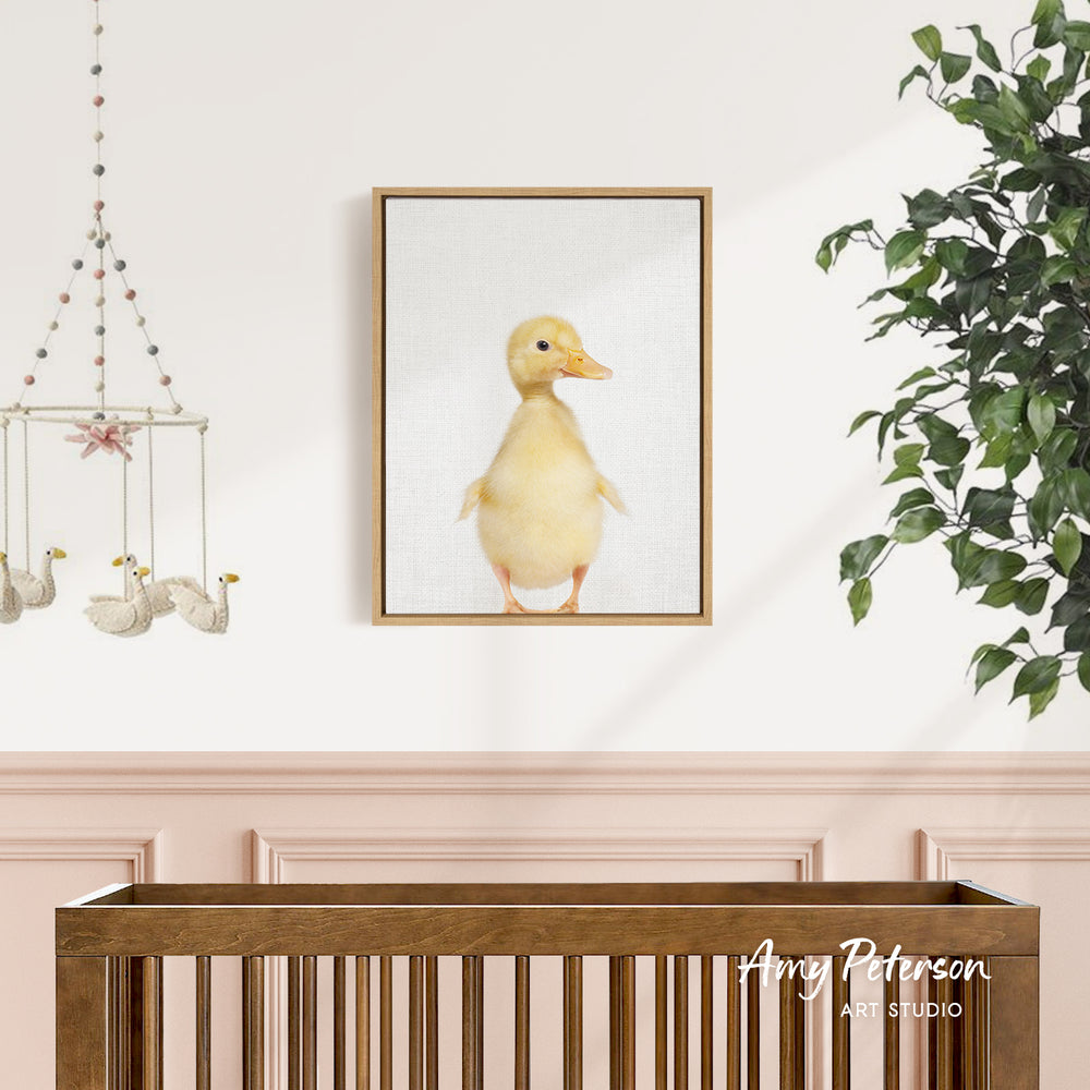 a baby's nursery with a wooden crib, a hanging mobile with white duck figures, and a framed picture of a yellow duck on the wall.