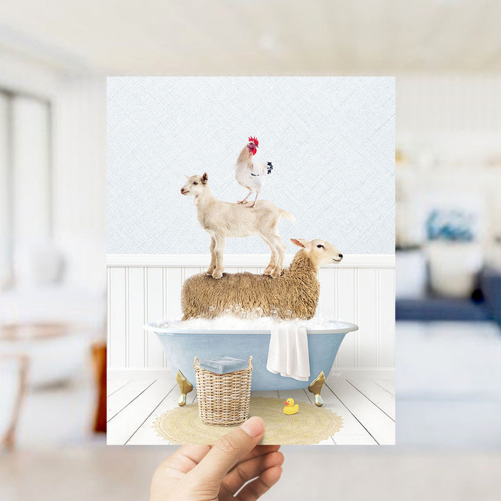 A hand holds up a framed image depicting a goat standing on a sheep's back while a chicken sits on top of the sheep. The scene is set in a bathroom, with a bathtub and a yellow rubber duck nearby.