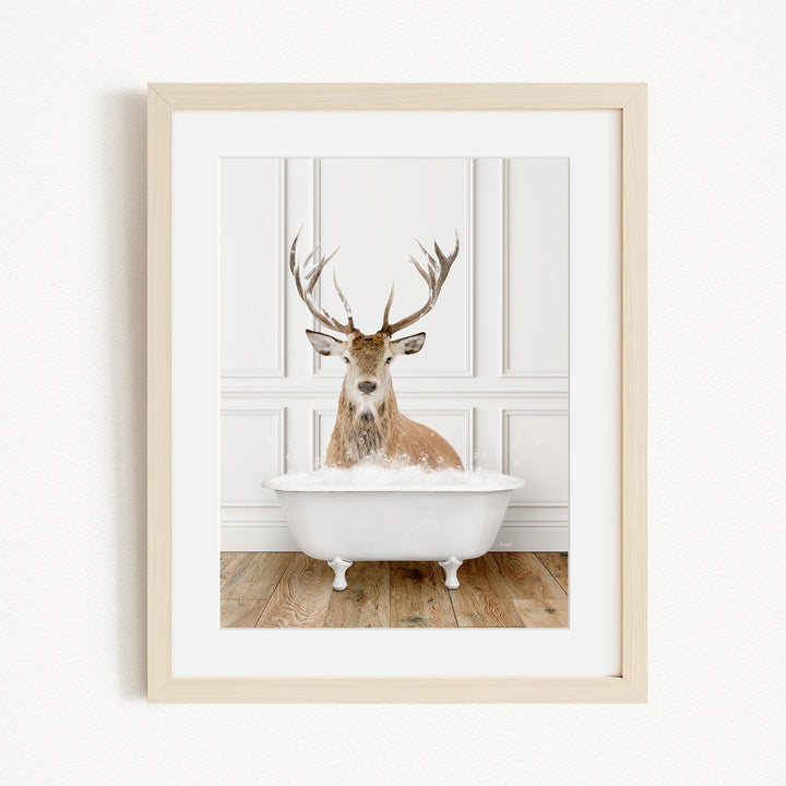 A deer with large antlers is sitting in a white bathtub filled with bubbles, creating a whimsical and unexpected scene.