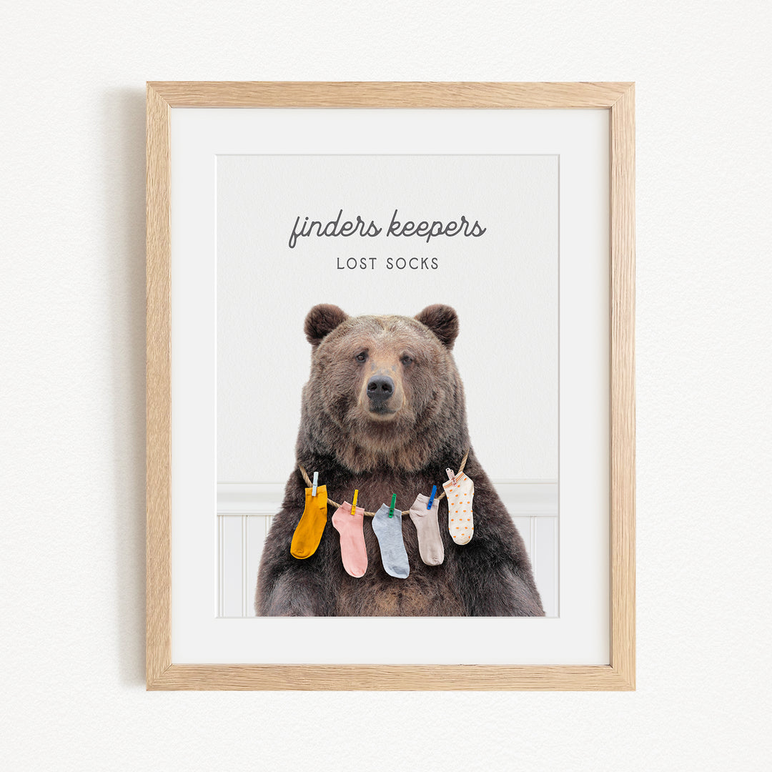 A framed image of a bear wearing socks, with the text "finders keepers" and "lost socks" above the bear.