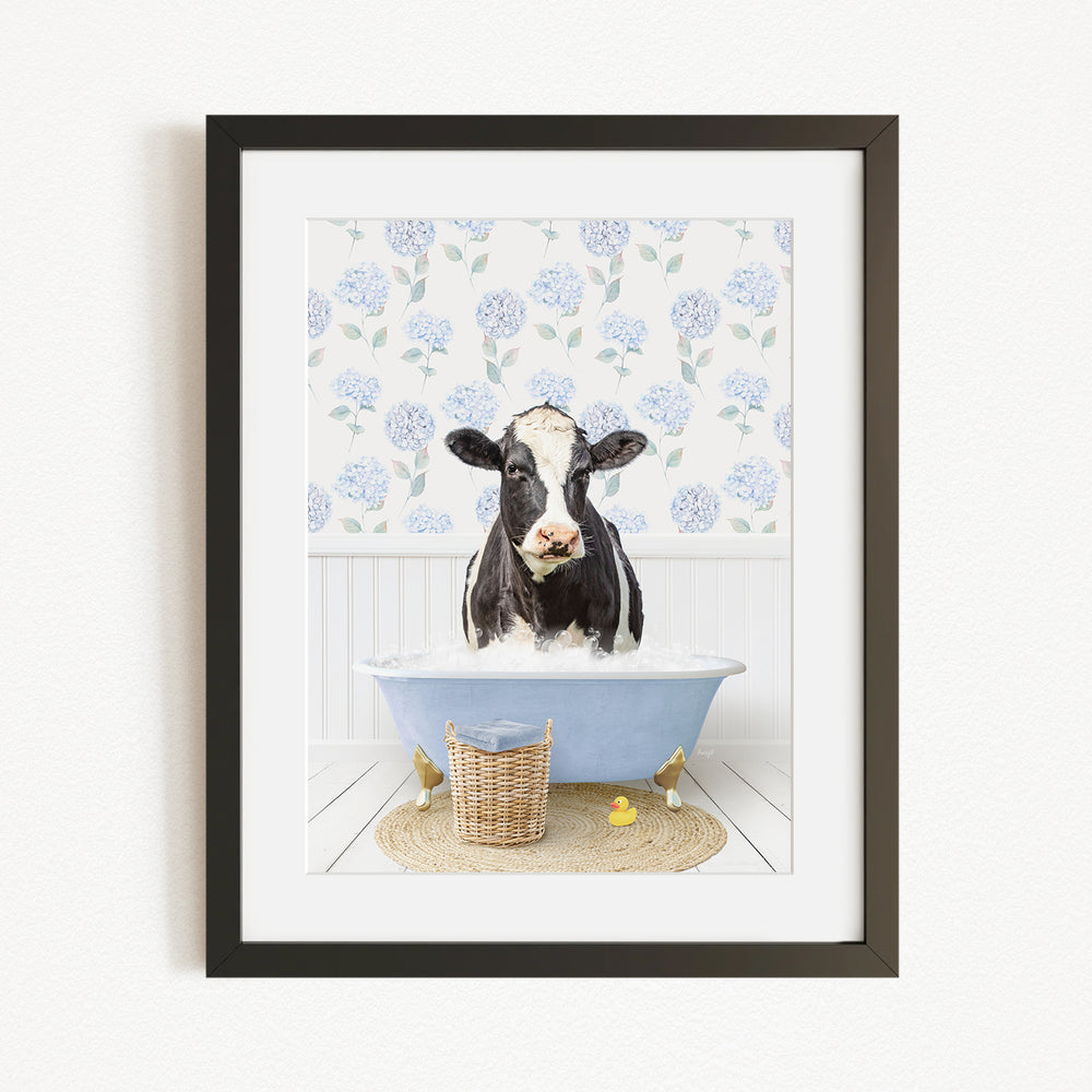 A black and white cow is sitting in a blue bathtub filled with water, surrounded by a floral patterned wall and a basket of rubber ducks.