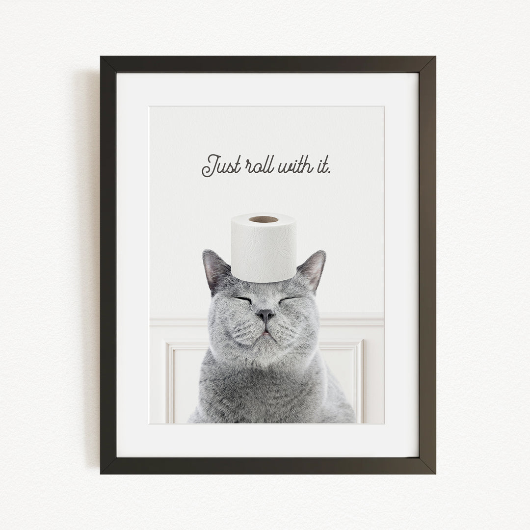 A gray cat with its eyes closed and a roll of toilet paper on its head, with the text "Just roll with it" above the cat.