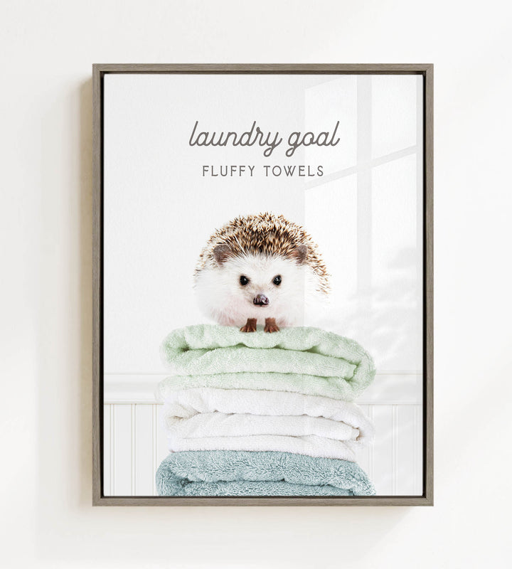 A framed image of a hedgehog sitting atop a stack of fluffy towels, with the text "laundry goal" and "FLUFFY TOWELS" written above it.