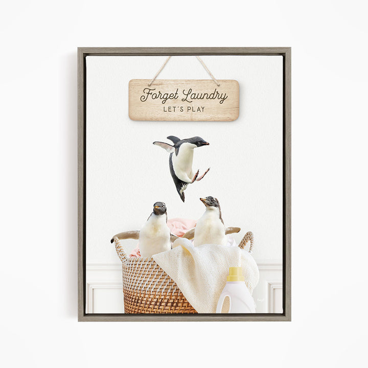 A framed image depicting three penguins in a basket, with a sign above that says "Forget Laundry, Let's Play".