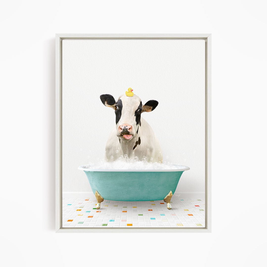 A cow is sitting in a blue bathtub filled with bubbles, with a yellow rubber duck perched on its head.