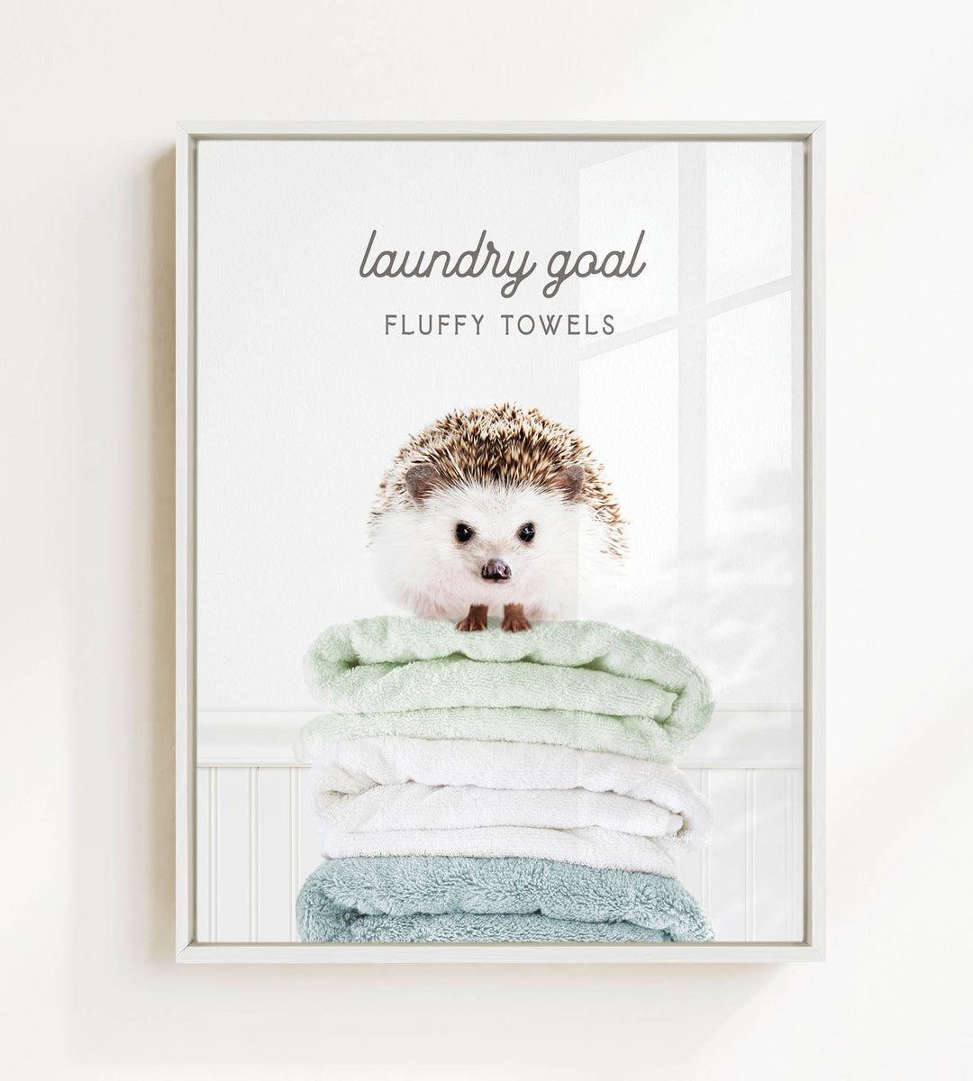 A framed image of a hedgehog sitting atop a stack of fluffy towels, with the text "laundry goal" and "FLUFFY TOWELS" displayed above the hedgehog.