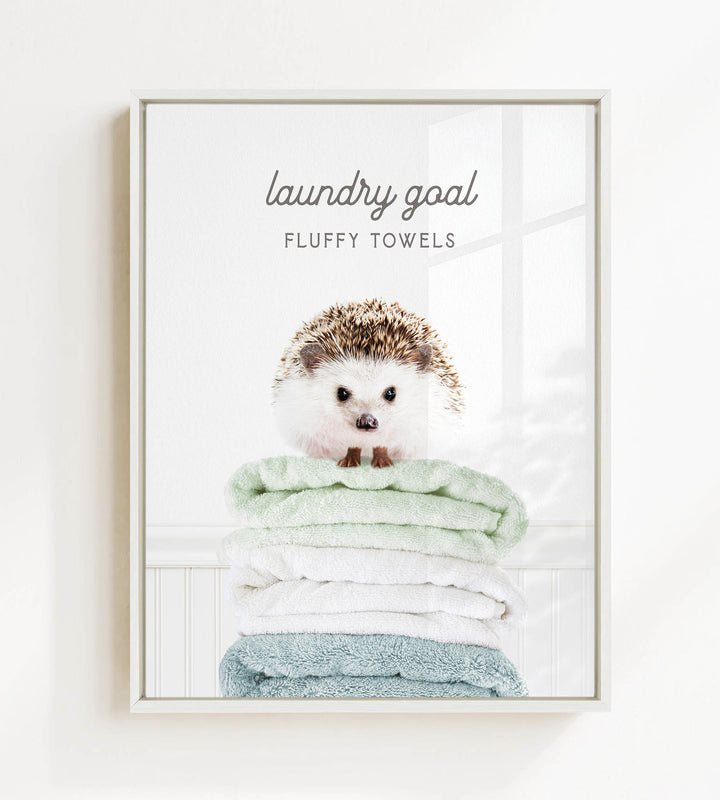 A framed image of a hedgehog sitting atop a stack of fluffy towels, with the text "laundry goal" and "FLUFFY TOWELS" displayed above the hedgehog.