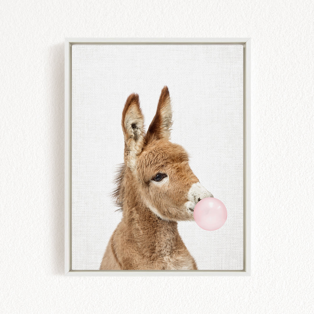 A brown donkey blowing a pink bubble with its nose.