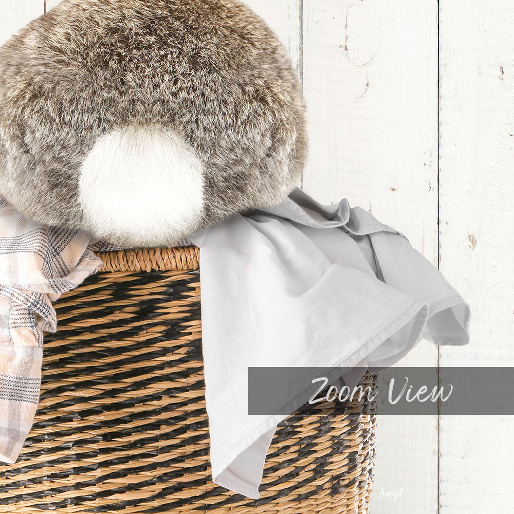 A cozy scene featuring a plush gray rabbit nestled in a woven basket, with a gray blanket and a plaid scarf nearby.