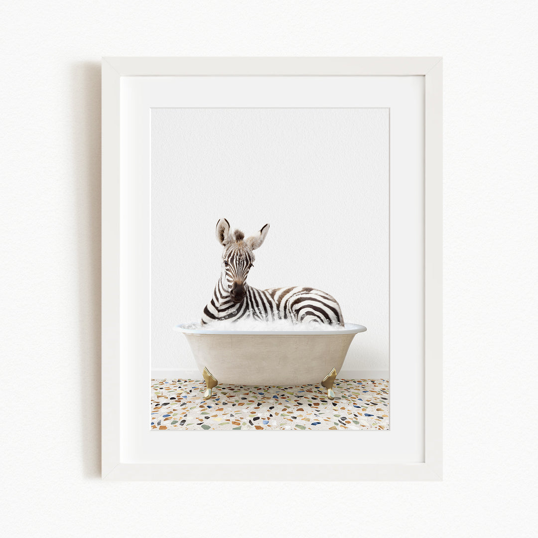 A zebra is sitting in a white bathtub, surrounded by a patterned floor.