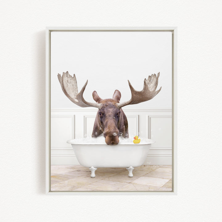 A moose with large antlers is sitting in a white bathtub, with a rubber duck floating in the water.