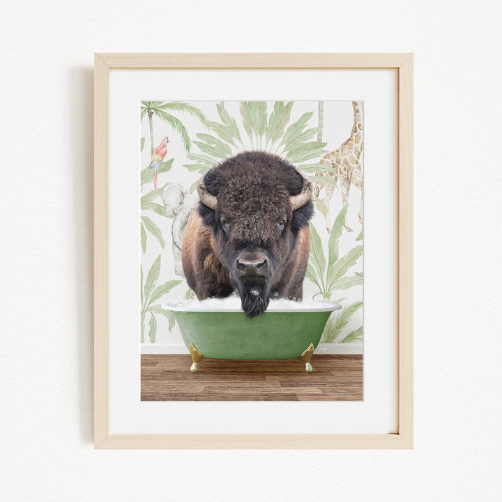 A buffalo is sitting in a green bathtub, surrounded by tropical foliage and a giraffe in the background.