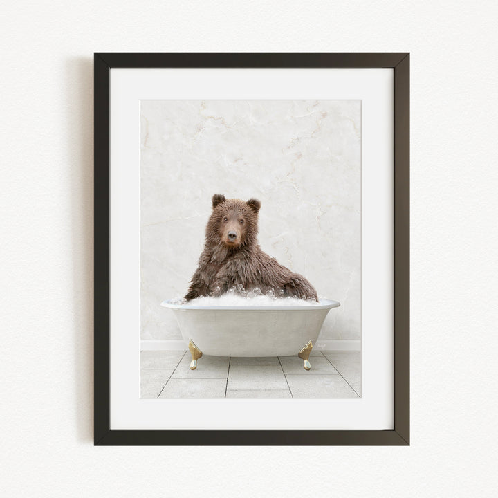 A brown bear sitting in a white bathtub filled with bubbles, looking directly at the camera.