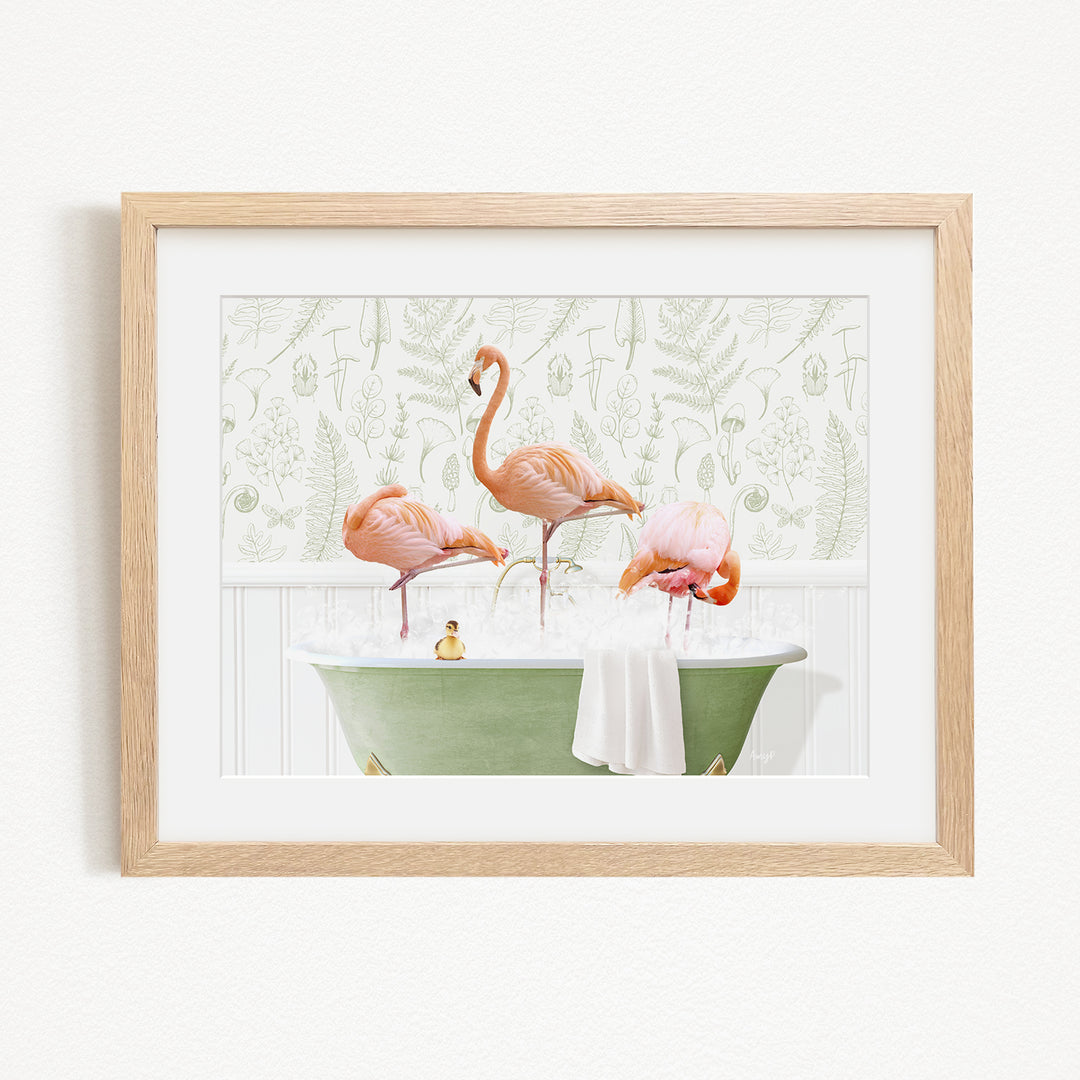 A framed image depicting three pink flamingos standing in a green bathtub filled with water, with a towel and a small toy duck floating on the surface.