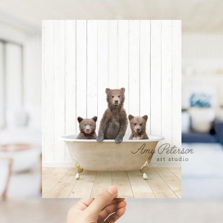 a hand holding a photo of three bears in a bathtub