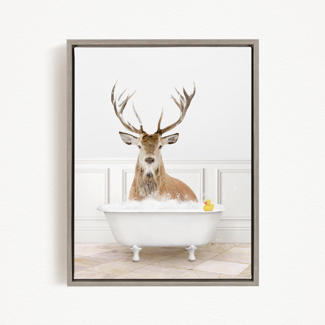 A deer with large antlers is sitting in a white bathtub filled with bubbles, with a yellow rubber duck floating in the water.