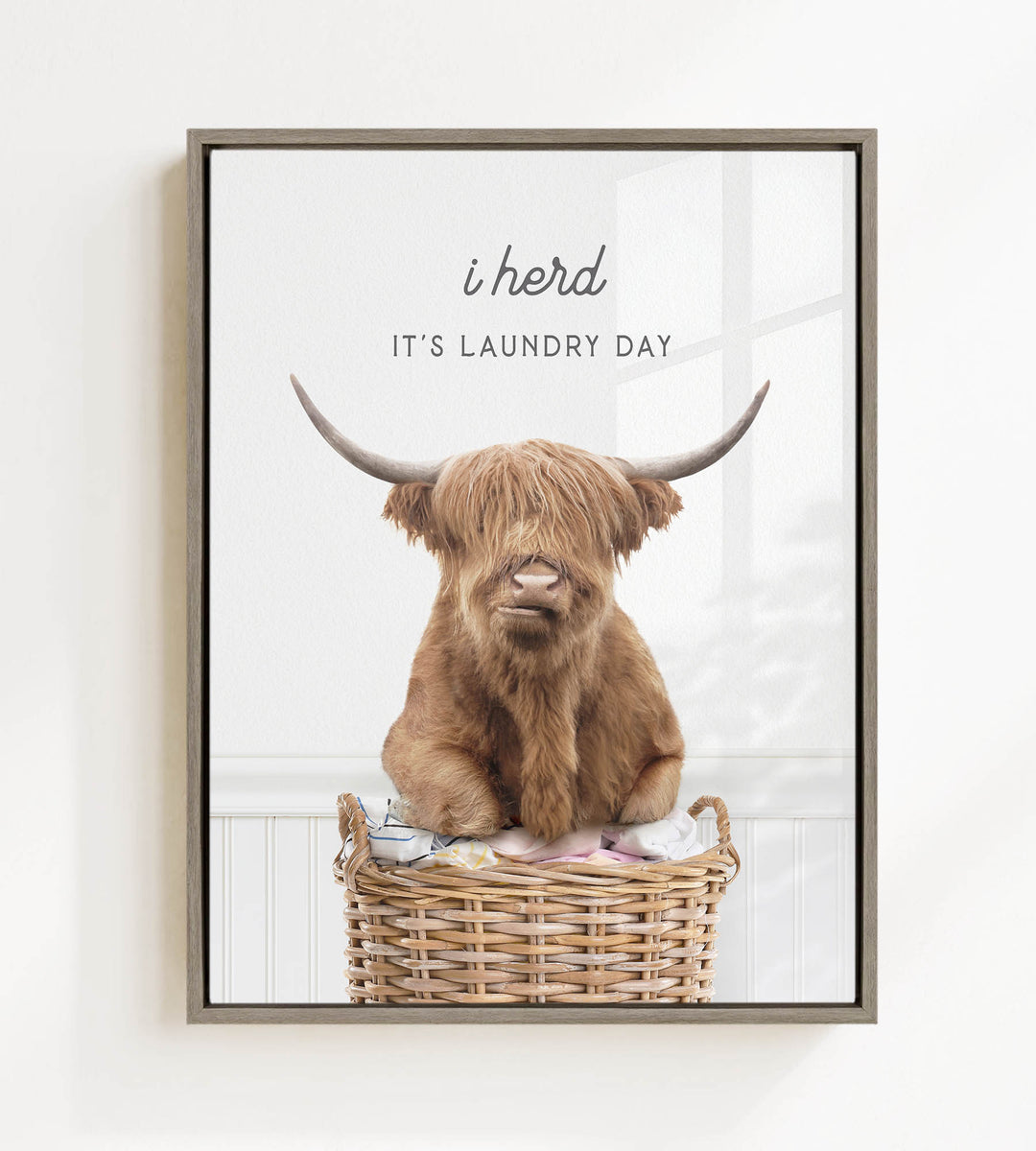 A brown cow with long horns is sitting in a wicker basket, with the text "i herd, it's laundry day" above the image.