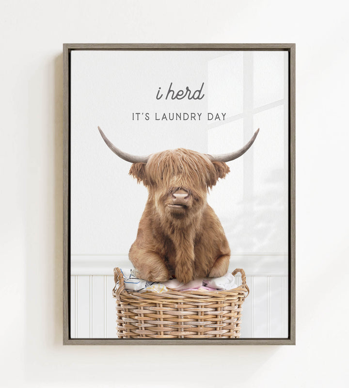 A brown cow with long horns is sitting in a wicker basket, with the text "i herd, it's laundry day" above the image.