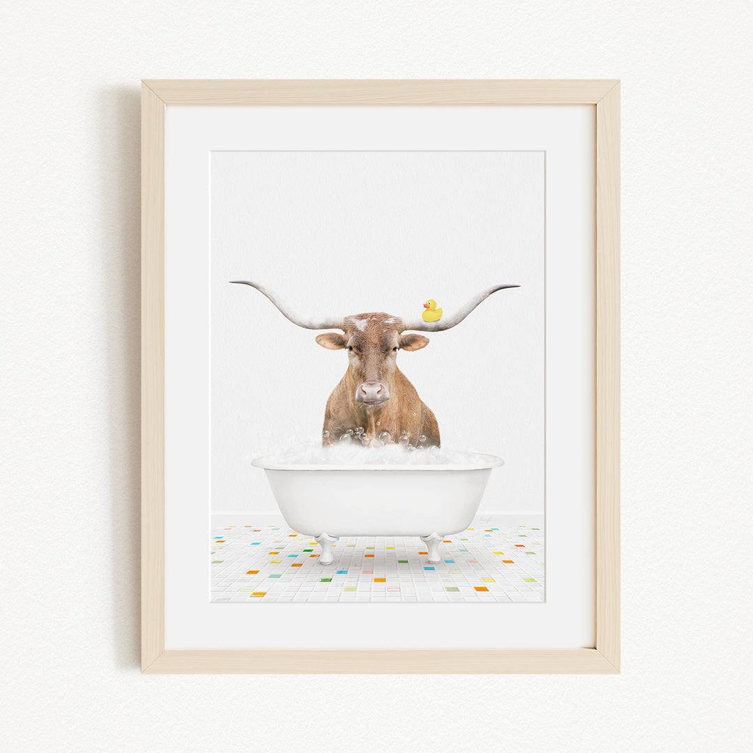 A brown cow with large horns is sitting in a white bathtub filled with bubbles, with a yellow duck perched on its head.