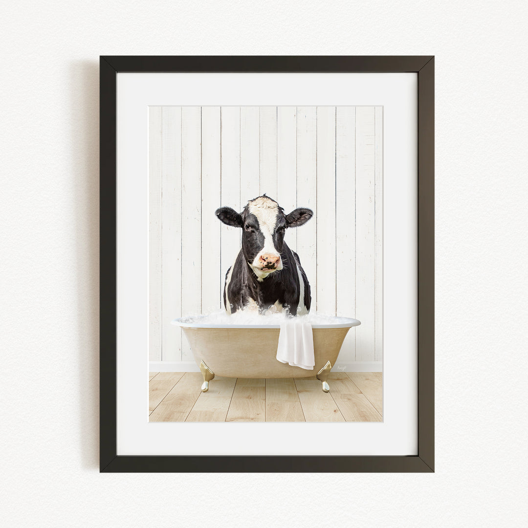 A black and white cow is sitting in a white bathtub filled with water, creating a whimsical and humorous scene.