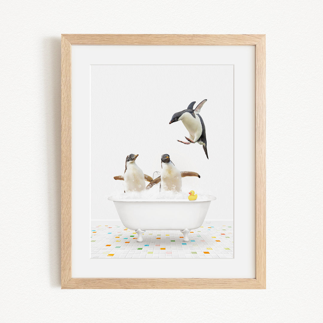 A framed image depicting two penguins sitting in a bathtub, with one penguin jumping out of the tub and another penguin sitting in the tub.