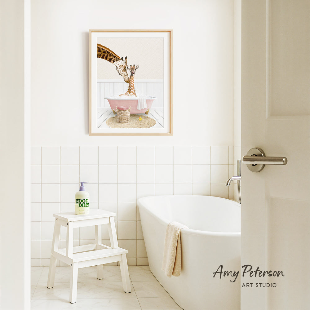 A framed image of a giraffe sitting in a pink bathtub is displayed on the wall above a white bathtub in a bathroom.