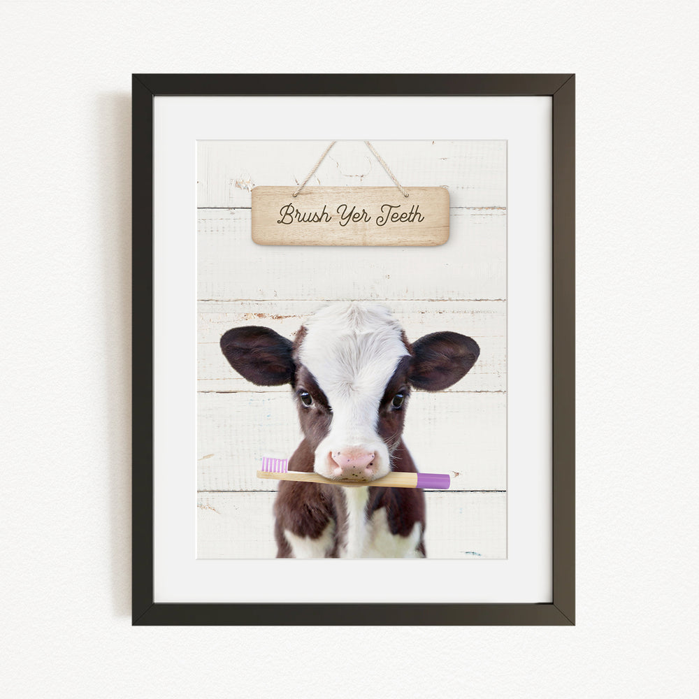 A framed image of a cow holding a toothbrush in its mouth, with a wooden sign above it that says "Brush Your Teeth".