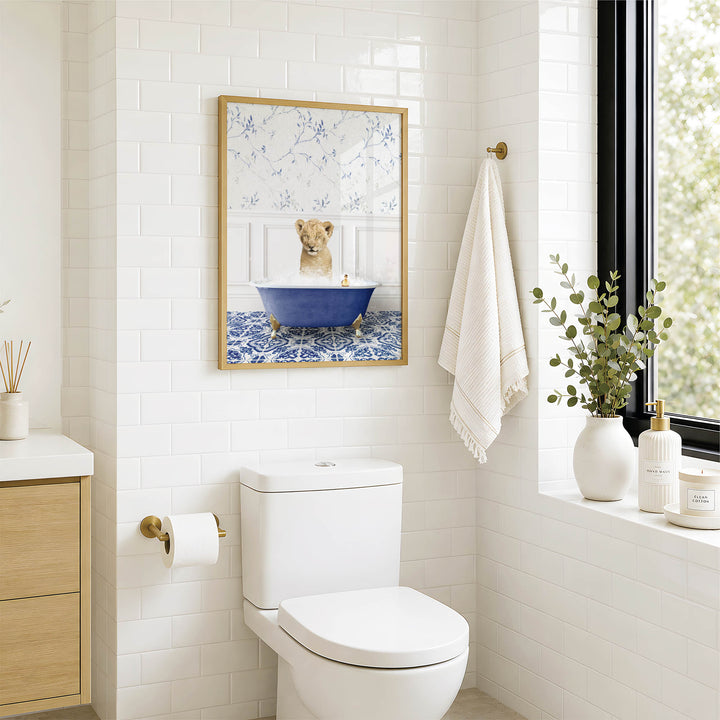A bathroom with a white toilet, a framed picture of a lion in a bathtub, and a window with greenery on the sill.