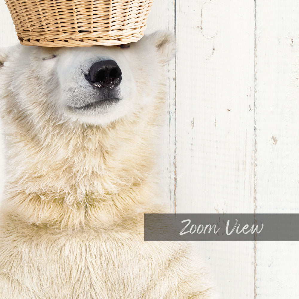 A close-up of a polar bear's face with a woven basket on its head, set against a white wooden background.