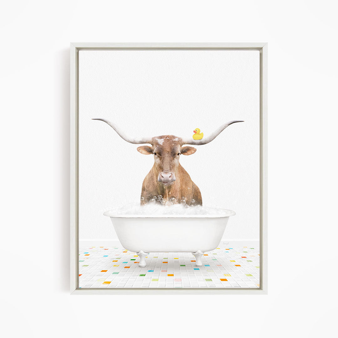 A brown cow with large horns is standing in a white bathtub filled with bubbles, with a yellow rubber duck floating on the water.