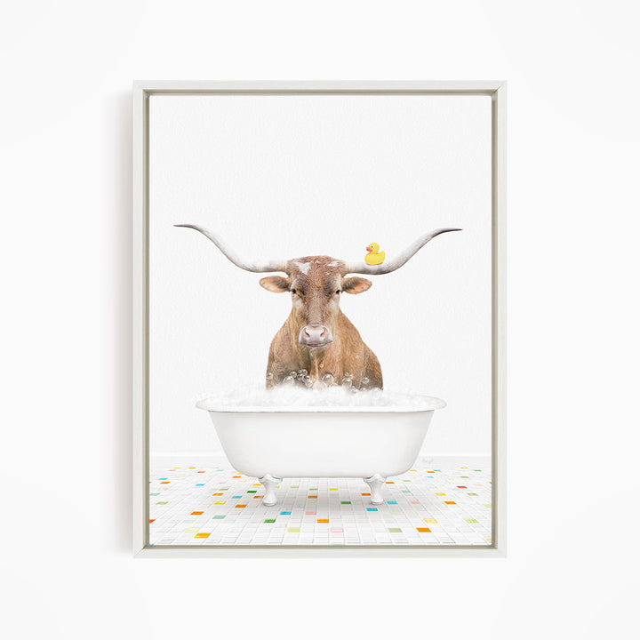 A brown cow with large horns is standing in a white bathtub filled with bubbles, with a yellow rubber duck floating on the water.