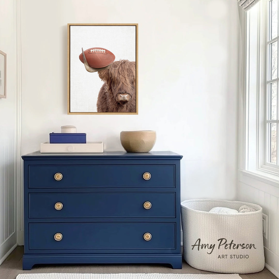 a blue dresser with a framed picture of a cow wearing a football hat on it, placed above a white basket.