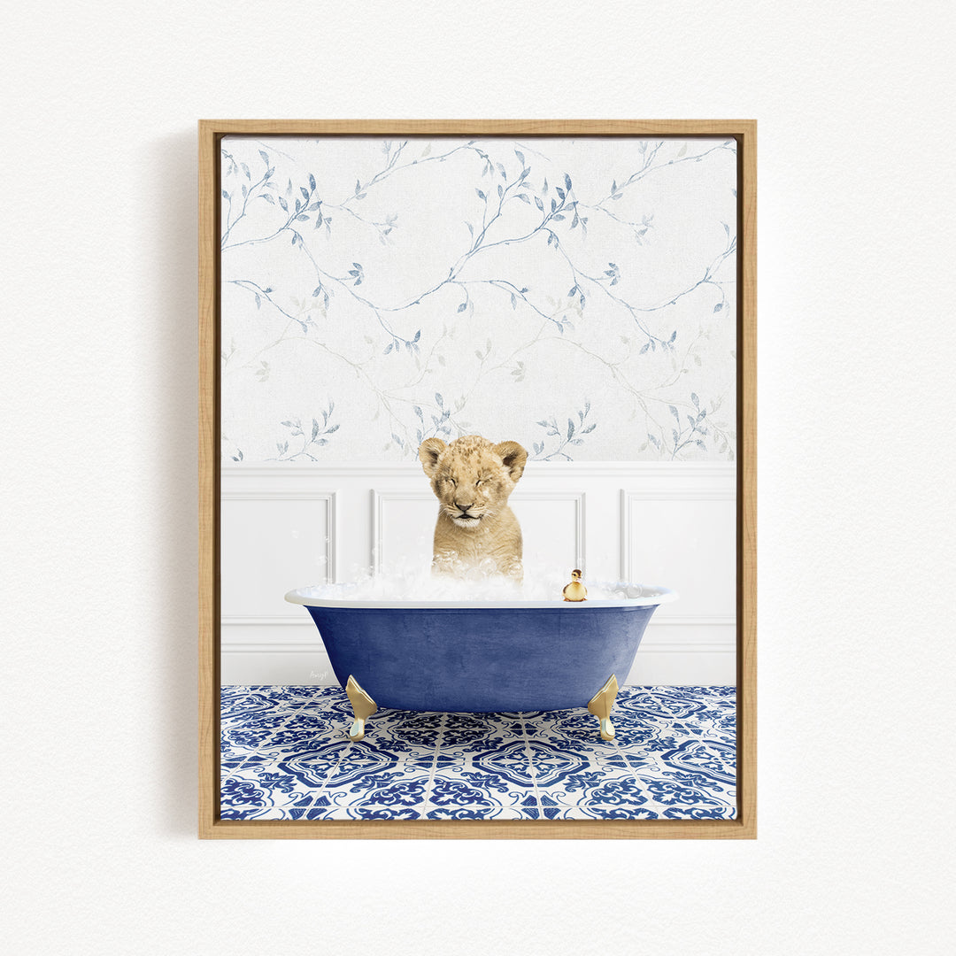 A young lion cub sitting in a blue bathtub filled with bubbles, surrounded by a blue and white patterned rug and a white wall with a floral pattern.