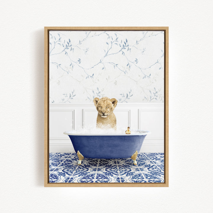 A young lion cub sitting in a blue bathtub filled with bubbles, surrounded by a blue and white patterned rug and a white wall with a floral pattern.