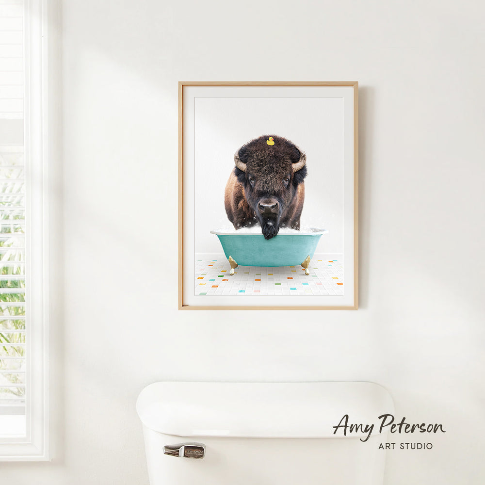 A framed image of a buffalo standing in a blue bathtub, with a white toilet in the foreground.