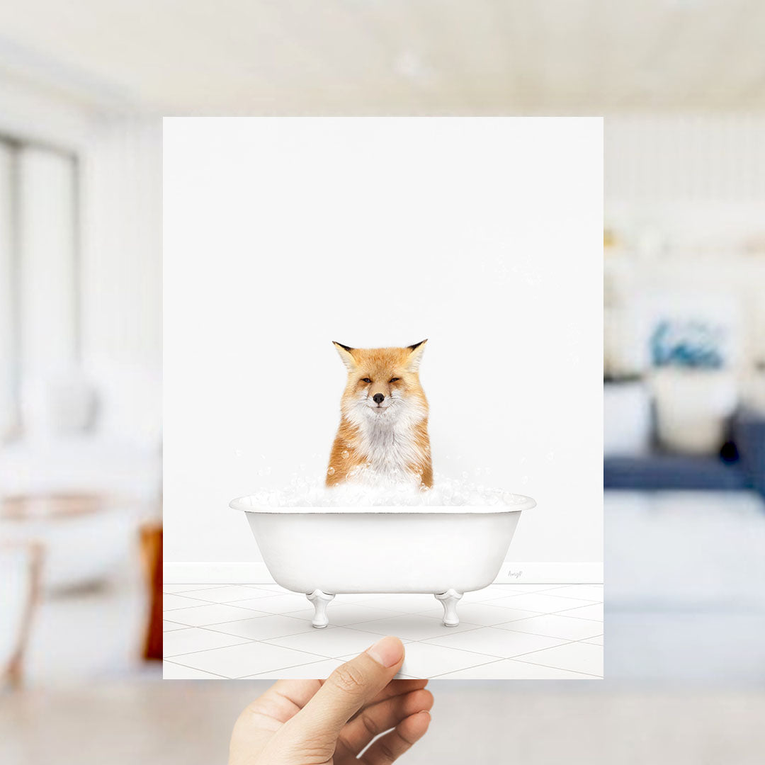 A hand holds up a framed image of a fox sitting in a bathtub filled with bubbles.
