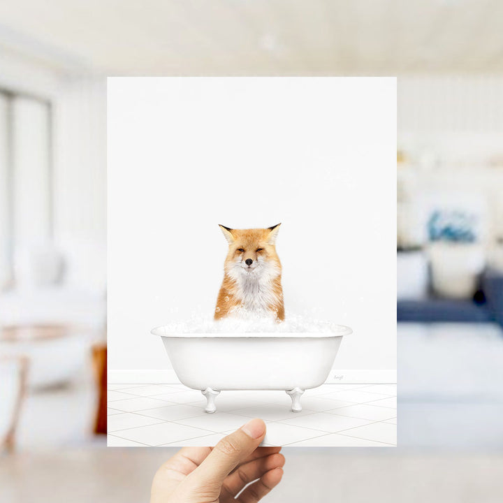 A hand holds up a framed image of a fox sitting in a bathtub filled with bubbles.