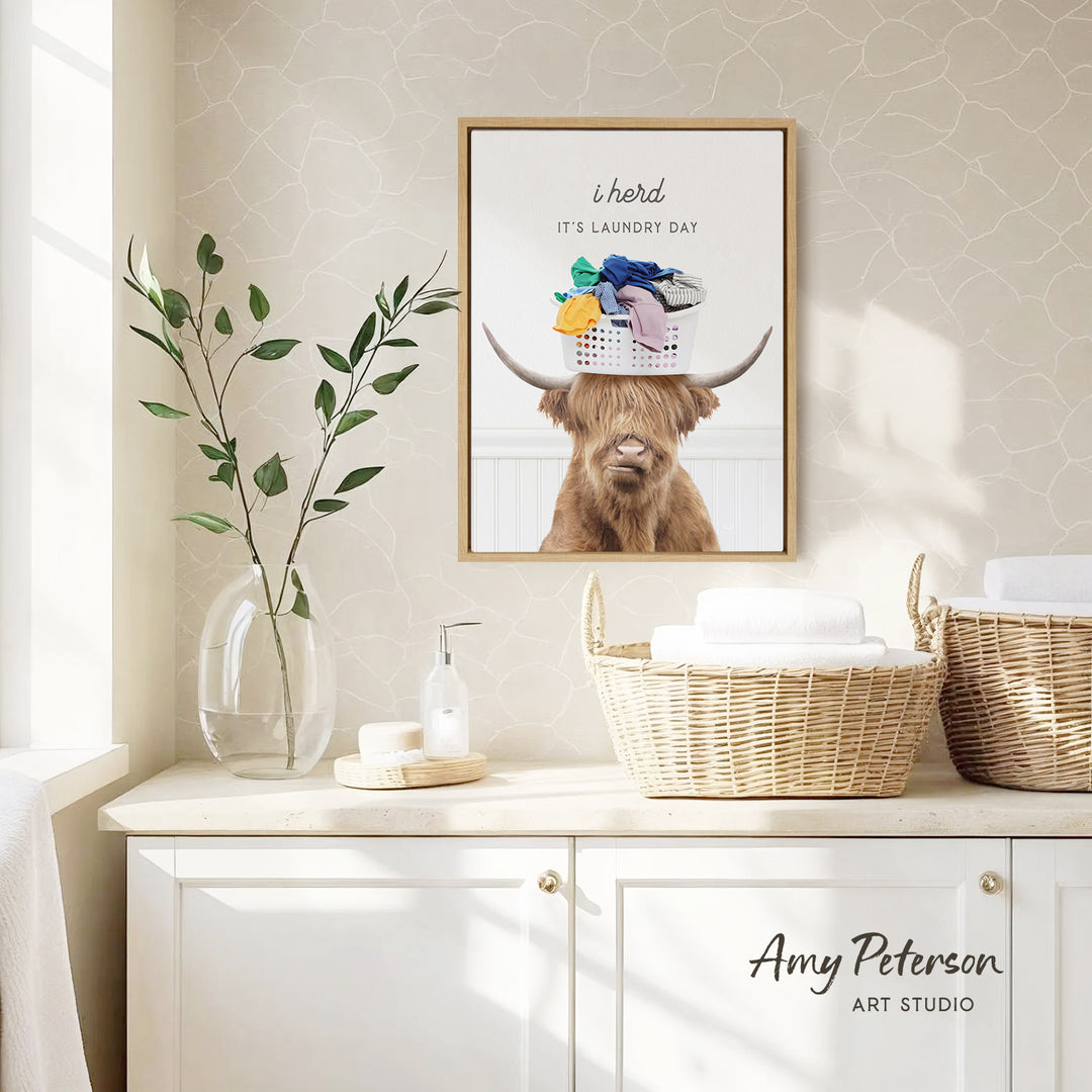 a framed poster of a Highland cow with horns, hanging on a wall above a white cabinet with baskets.