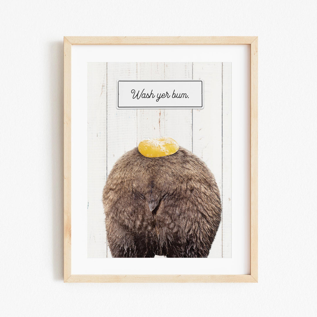 a wooden frame with a framed picture of a bear sitting on its back with a yellow object on its head, and a sign above it that says "Wash your butt."
